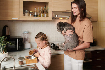 Smiling woman lifting dog to show her how girl filling bowl with food
