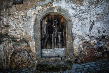 Fototapeta premium Facade Of An Abandoned House With An Old Patched Wooden Door. Abandoned Houses. Image With Texture And Copy Space. Evicted Housing Concept