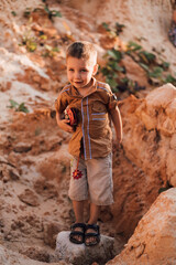 A little boy stands in the middle of the sand and holding a toy in his hands