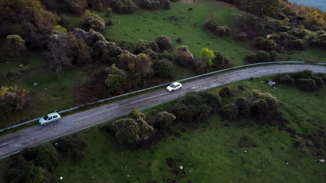 Drone footage of a car traveling on a mountain road in the middle of green meadows