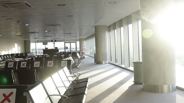 Airport during the Covid-19 pandemic. The rising sun in the morning illuminates the empty departure and waiting area from a chair with special social distancing signs