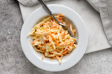 Traditional coleslaw salad with fresh sliced carrots and cabbage in a white bowl with copy space. Cole slaw