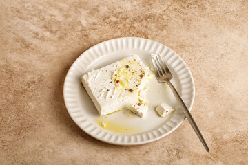 Natural marinated greek feta cheese on white plate with olive oil and herbs, pepper. Fork, beige...