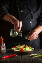 Professional chef pours olive oil into a bowl of salad. Cooking tasty and healthy food with set of vitamins. Recipe for hotel