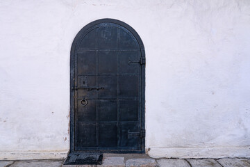 Fragment of the wall of an old stone building covered with white plaster. There is a black iron...