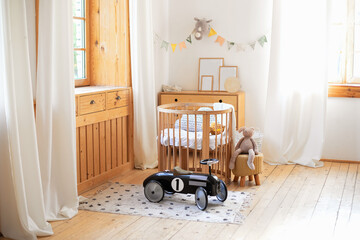 Modern interior of a children's bedroom. Copy space. Hygge. Kindergarten. Cozy Scandinavian lights baby room: wooden crib with bedding and plush toys. Retro style child toy racing car in children room © stock_studio