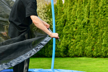 The guy collects a new trampoline at home and pulls on a protective net.