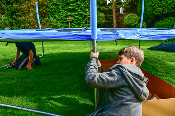 Children build a new trampoline at home and stretch the trampoline fabric with springs.