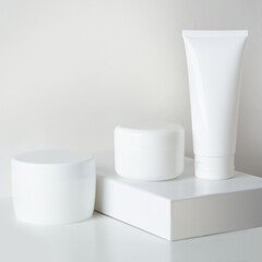 different white boxes of body cream on a pedestal on a light background