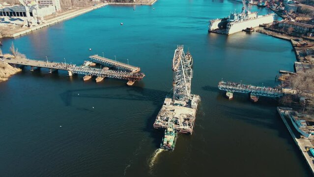 Powerful tugboat pulling floating crane by river in city of shipbuilders. Logistics concept of water cargo transportation