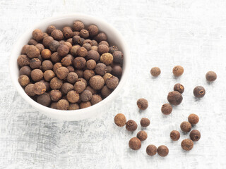 Spice Allspice (Jamaica pepper, Pimento) in white ceramic bowl and bunch on white concrete...