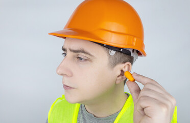 A worker in a hard hat and green vest puts on ear plugs. Industrial safety. Industrial noise protection. Compliance with the rules of conduct at loud work. Orange ear plugs