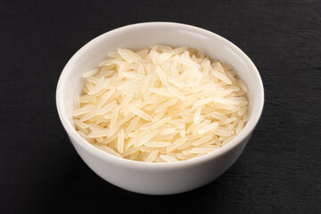Long Basmati rice in ceramic bowl on black wooden background. Macro. Vegetarian food concept