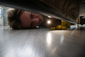 Woman using flashlight to look for something under bed - obrazy, fototapety, plakaty