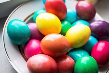 painted multi-colored chicken eggs in a wide white plate as a symbol of the holiday of Catholic...