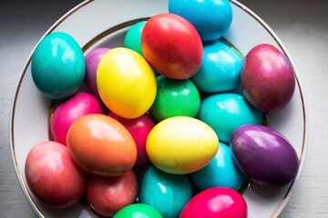 painted multi-colored chicken eggs in a wide white plate as a symbol of the holiday of Catholic...