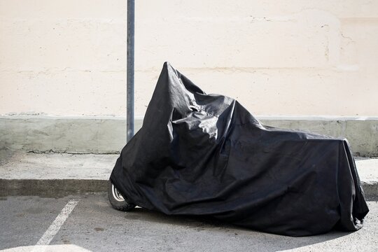 A Rare Motorcycle Is Hidden From Prying Eyes By A Black Cover Next To A Disabled Sign In The Parking Lot Near The House