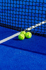 Three balls near the net of a blue padel tennis court