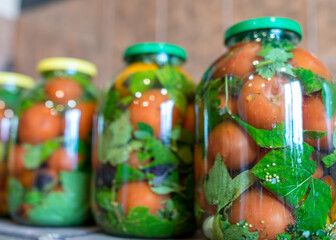 red tomatoes and green spices in glass jars, canned vegetables, tomato pickling, winter products, healthy diet, vegetarian diet, autumn harvest time