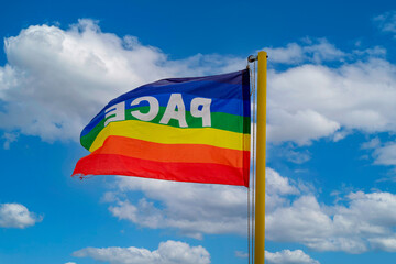 Peace flag waving. The flag in the colors of peace flutters against the backdrop of a cloudy blue sky. Symbol of peace in this time of war. pro concordia labor
