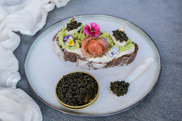 Delicious luxurious meal. Black Caviar Smoked Salmon Avocado Toast with Edible Flowers.