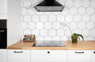 Modern kitchen with white cabinets, black hob and geometric tiles. Blooming orchid in the interior of the kitchen. Biophilic design.
