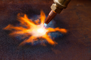 Gas cutting of metal. Gas cutter with copper nozzle with a stream of fire directed at the metal. Heating up the metal with a gas cutter.