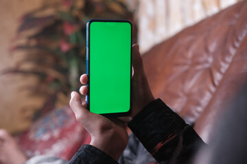  young man hand using smart phone with green screen lying on sofa 