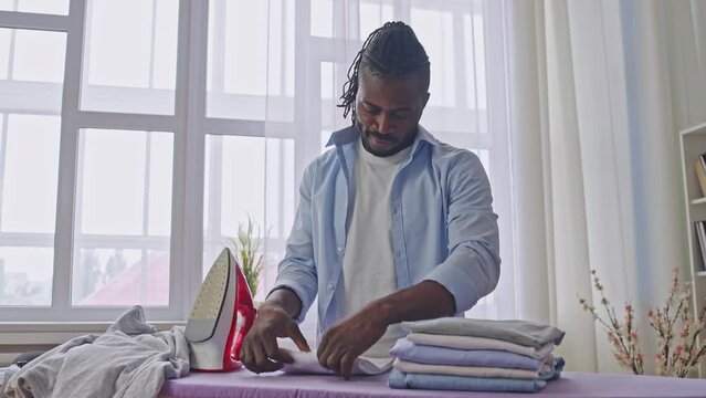 African american man carefully folding ironed clothes, enjoying neatness