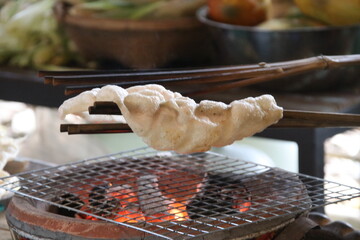 A indigenous rice cracker is roasting over fire from native clay stove, Thailand.
