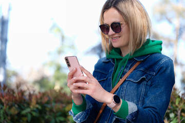 Smiling woman looks at phone on street