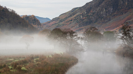 Stunning Autumn landscape sunrise image looking towards Borrowdale Valley from Manesty Park in Lake District with fog rolling across the landscape
