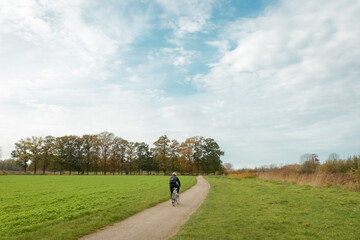 Fototapeta premium A cyclist drives through fields and forest country site. Beautiful autumn landscape with a cyclist