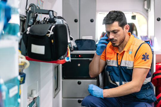 Young And Handsome Paramedic Talking On The Phone Inside An Ambulance Ready To Attend To An Emergency