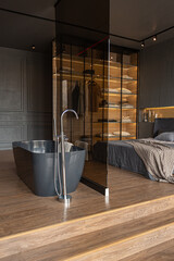 bedroom and freestanding bath behind a glass partition in a chic expensive interior of a luxury home with a dark modern design with wood trim and led light