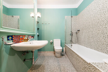 Bathroom with white porcelain hanging sink, large green-framed mirror, and glass-enclosed tub with tile tiles