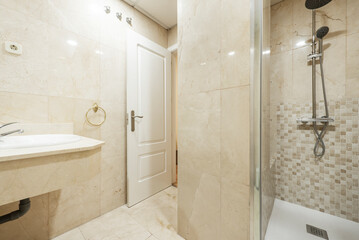 Bathroom with porcelain sink on cream-colored marble pendant countertop and built-in shower cabin with glass door