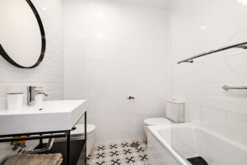 Bathroom with white porcelain sink on black metal cabinet, matching circular mirror and bathtub with glass partition