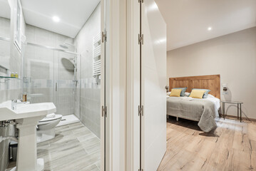 Fototapeta na wymiar En-suite bathroom with shower cabin, double bed with wooden headboard and chestnut wood floors