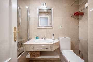 Bathroom with cream marble countertop to match the walls, mirror with silver frame and shower cabin with glass partition