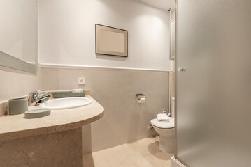 Fototapeta na wymiar Bathroom with cream marble washbasin to match the floors, framed mirror, plaster border on the wall and shower cubicle with glass partition