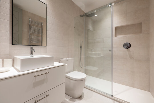 Bathroom with white porcelain sink on white chest of drawers, black framed mirror and glass sliding shower stall