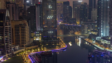 Dubai Marina with several boats and yachts parked in harbor and skyscrapers around canal aerial night to day timelapse.