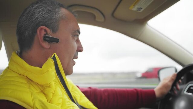 Mid age caucasian man driving car and talking with wireless earphones. Taxi driver concept 