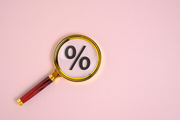 Percentage sign under magnifying glass, on pink background.