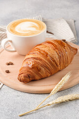 Large croissant and a cup of cappuccino on a light background