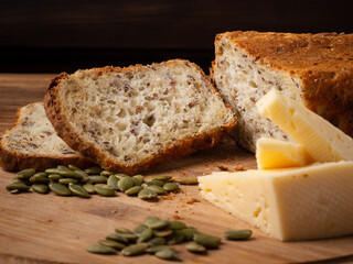 Cereal bread on a wooden board with cheese and pumpkin seeds