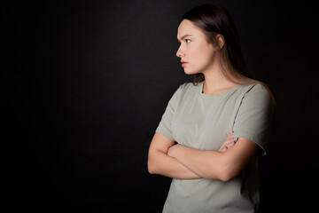 Obraz premium Suspicions, a look from the left. A young brunette woman in a T-shirt, experiencing distrust and doubt, portrait on black