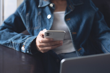 Young casual business woman sitting on a sofa using mobile phone and laptop computer at home, close up