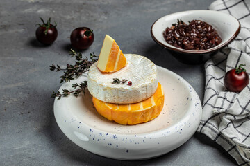 Camembert, Brie, Gorgonzola and blue cream cheese with thyme and onion marmalade jam. French cuisine. An aperitif on a gray background